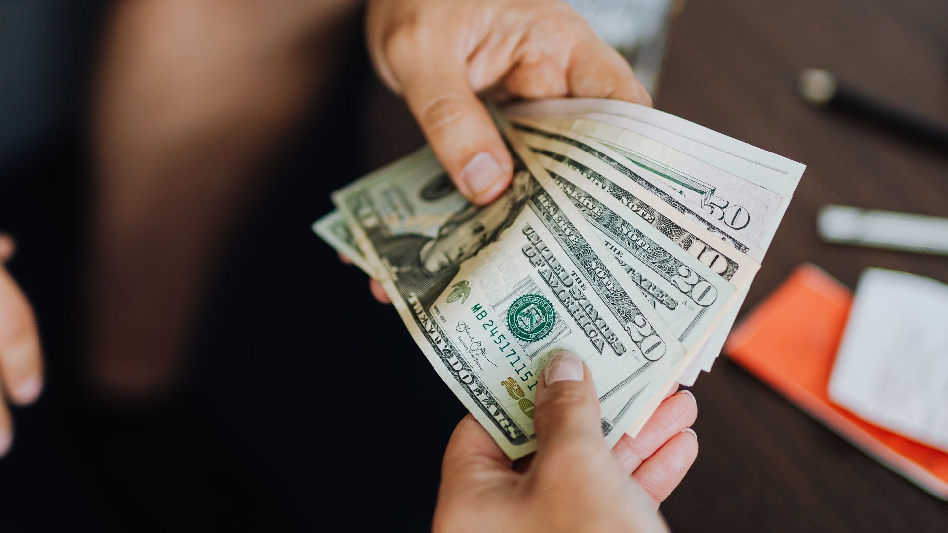 A close-up view of hands exchanging dollar bills indoors, symbolizing payment.