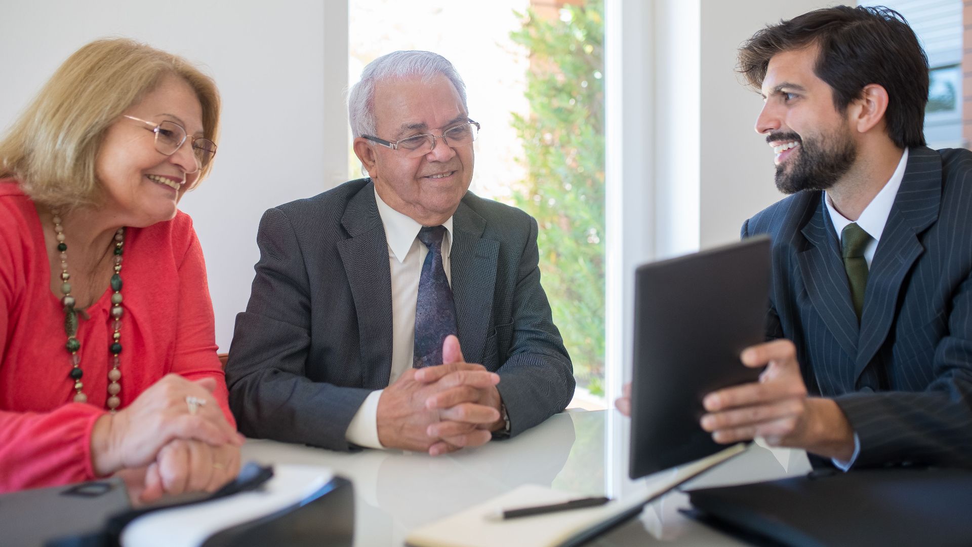 Elderly couple discussing real estate options with an agent in a modern office setting.