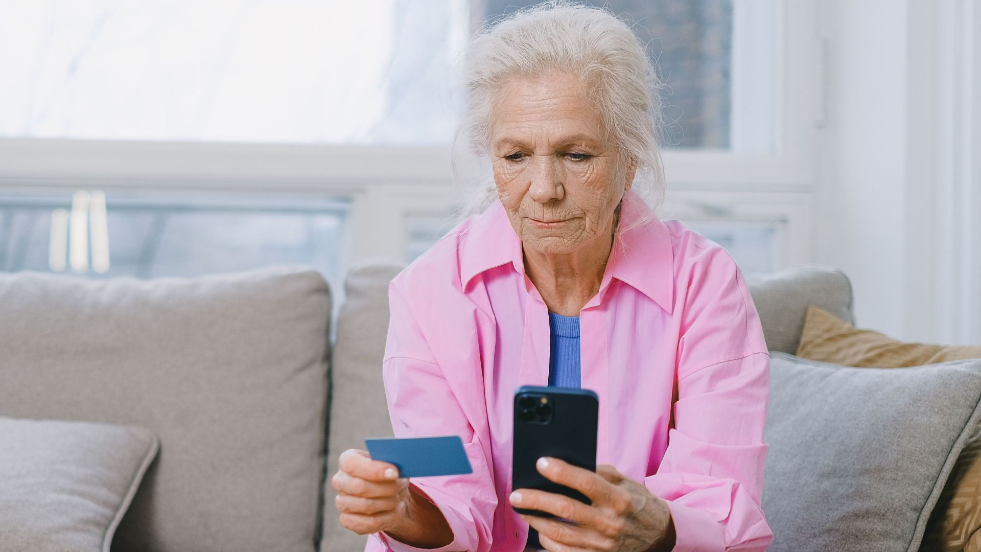 Elderly woman shopping online using smartphone and credit card indoors.