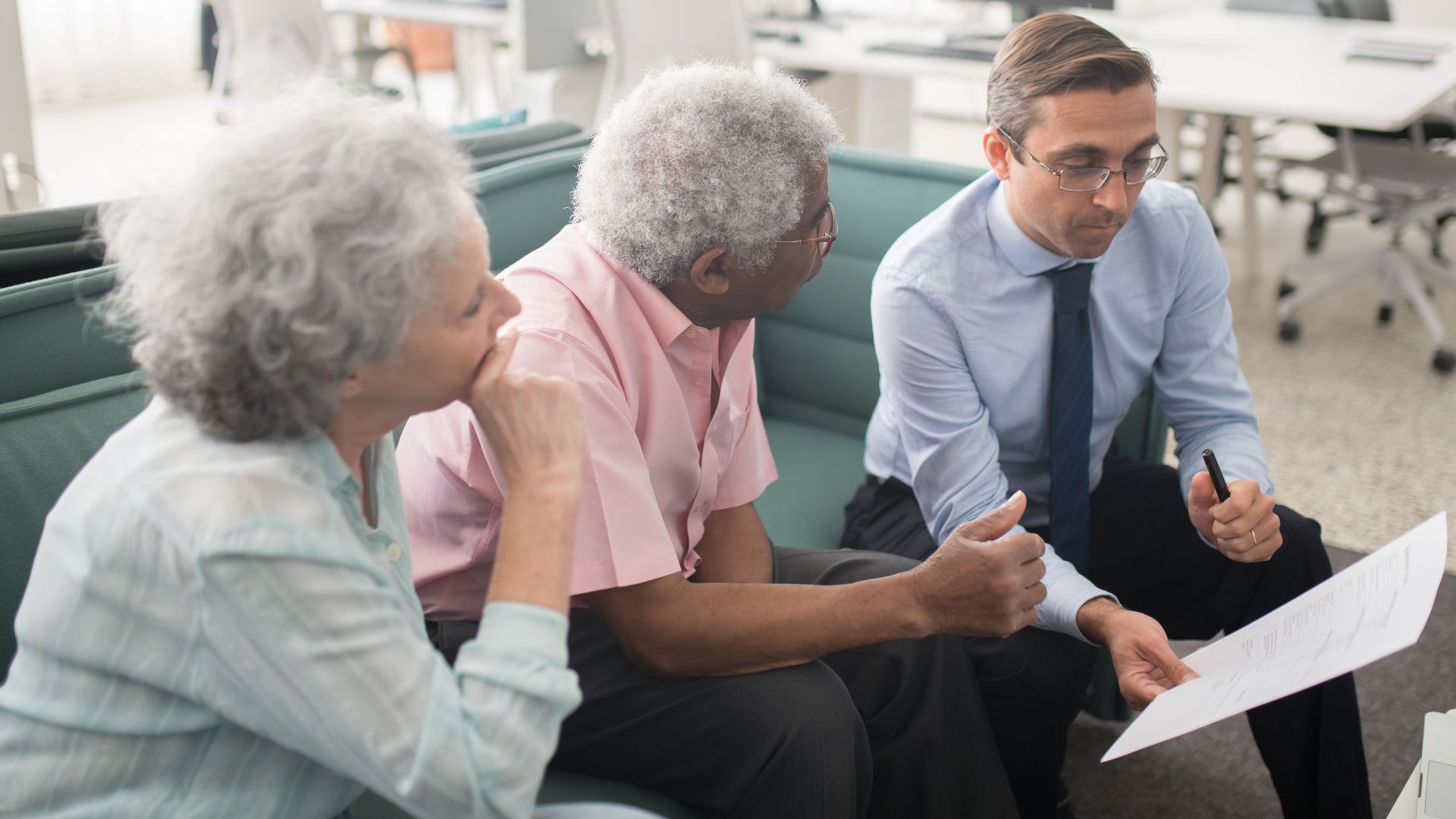 Business professional consults elderly clients in an office setting. Collaborative discussion, paperwork visible.