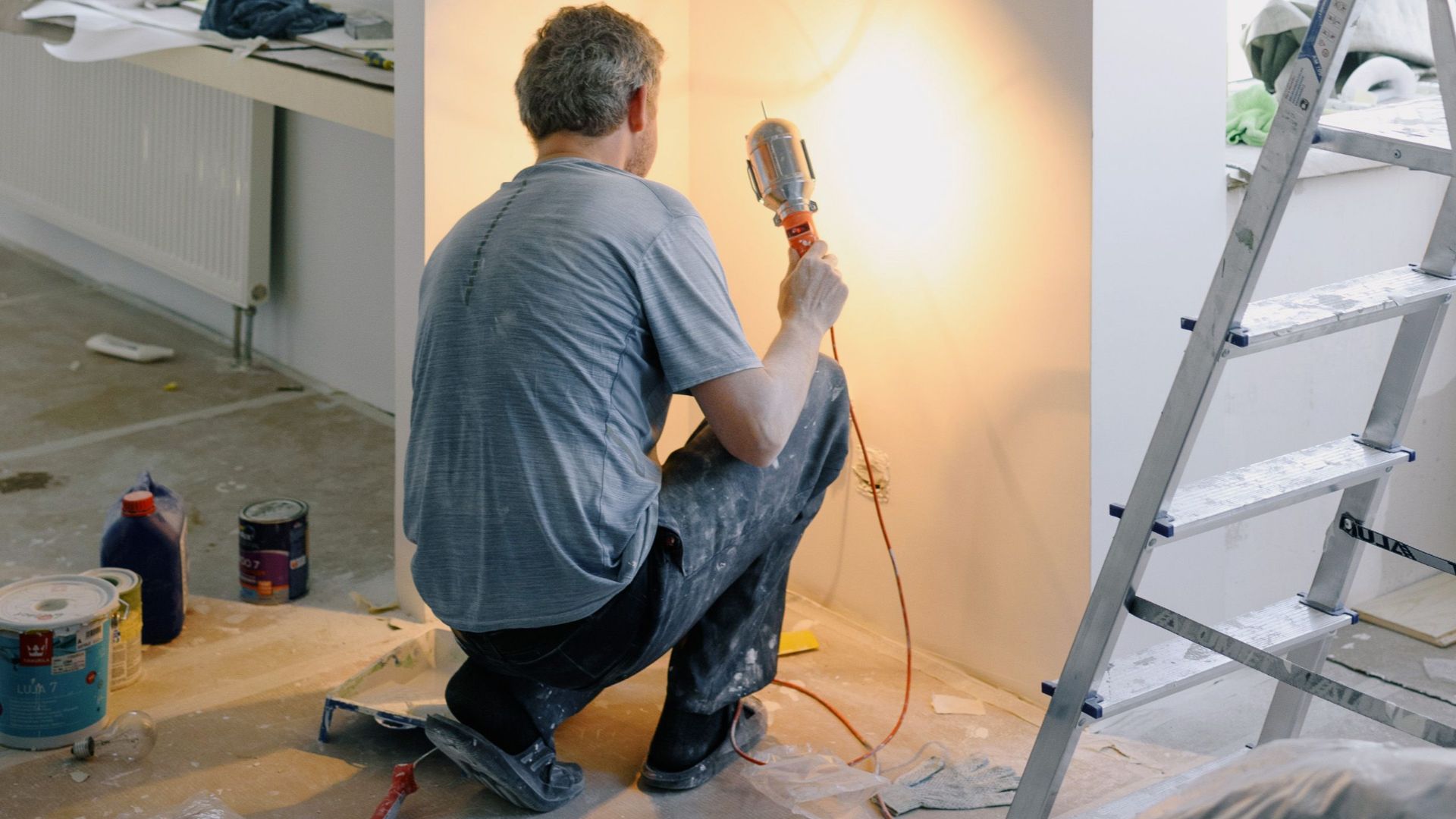Back view of anonymous male in dirty clothes renovating walls in home while holding lamp