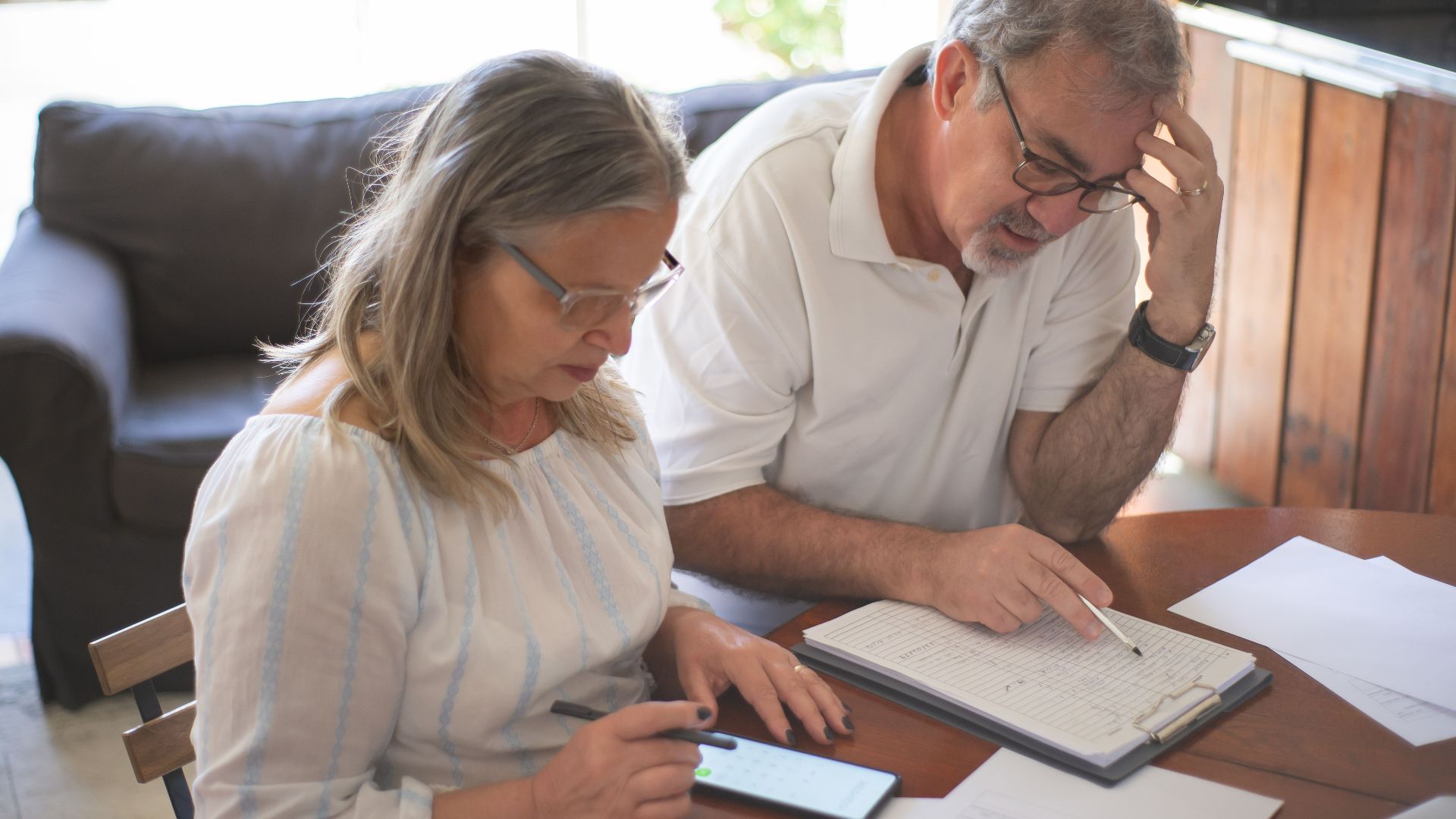 Elderly couple reviewing bills and documents at home, focusing on finances and technology.