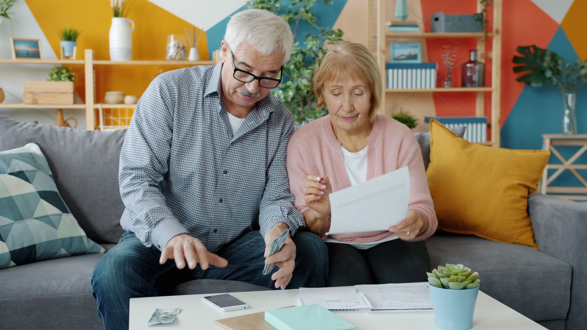 Elderly couple planning their budget, reviewing documents in a cozy living room.