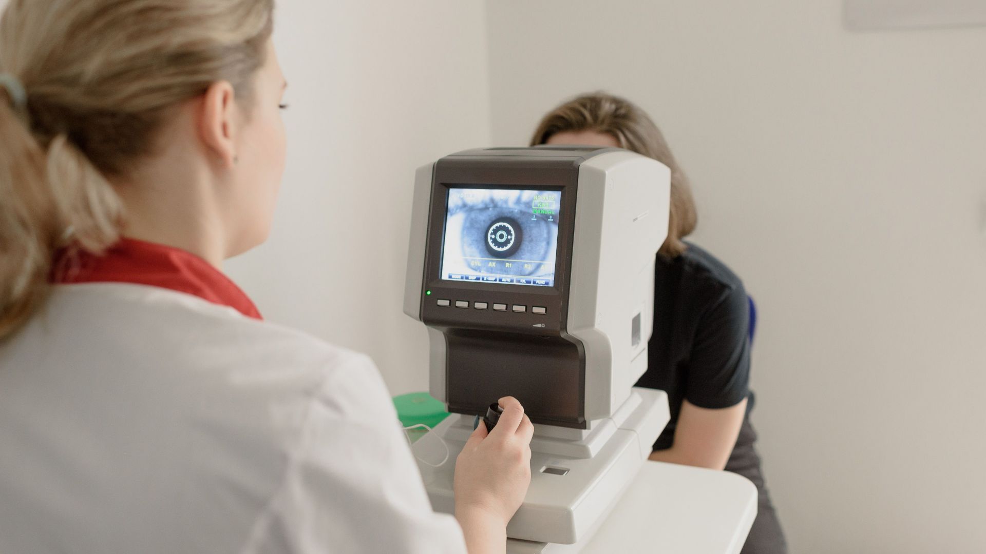 Unrecognizable ophthalmologist checking eyesight of female on vision screener with eye illustration on display in clinic