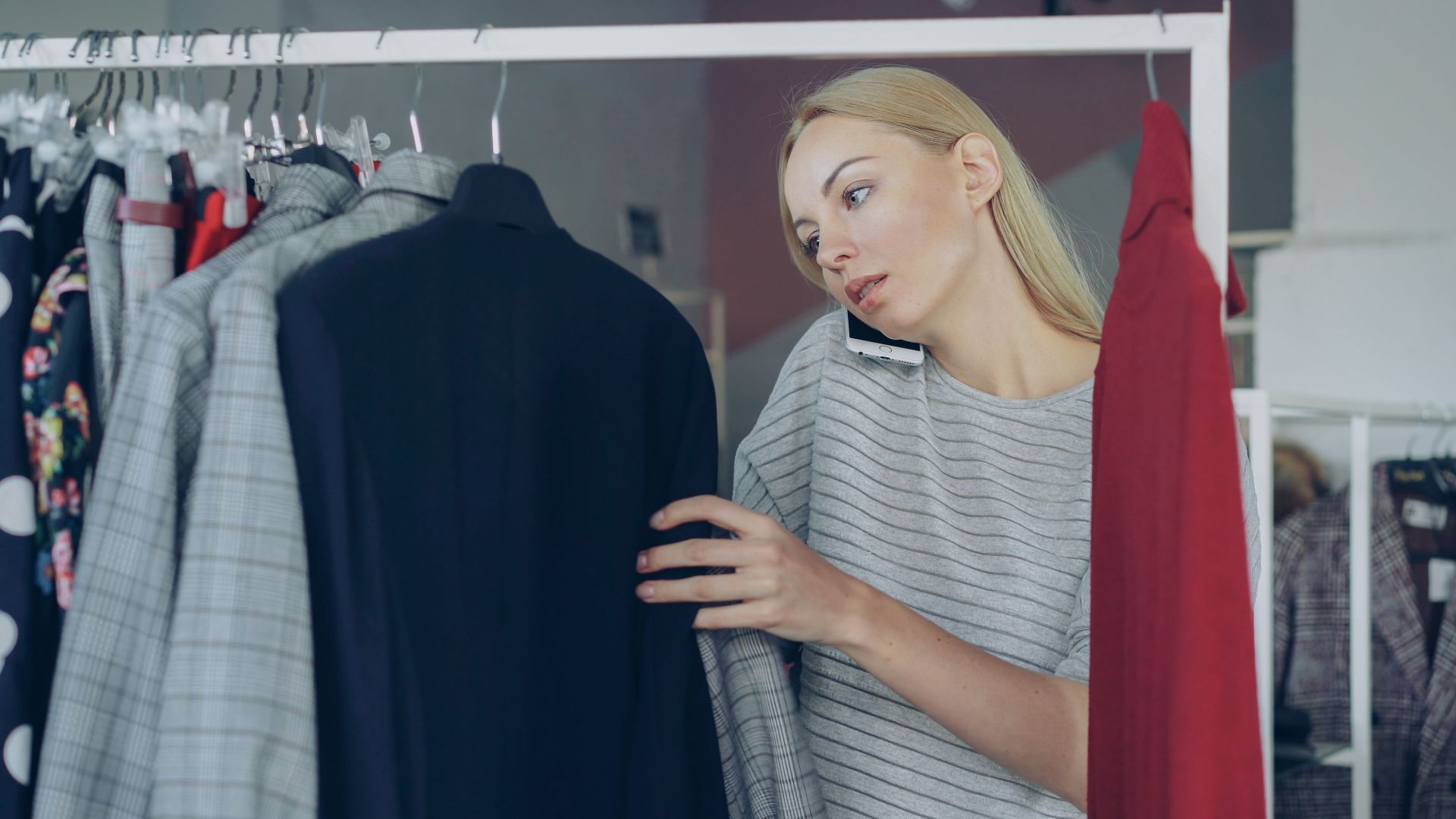 Woman browsing clothes while talking on phone in a store. Multitasking and fashion concept.