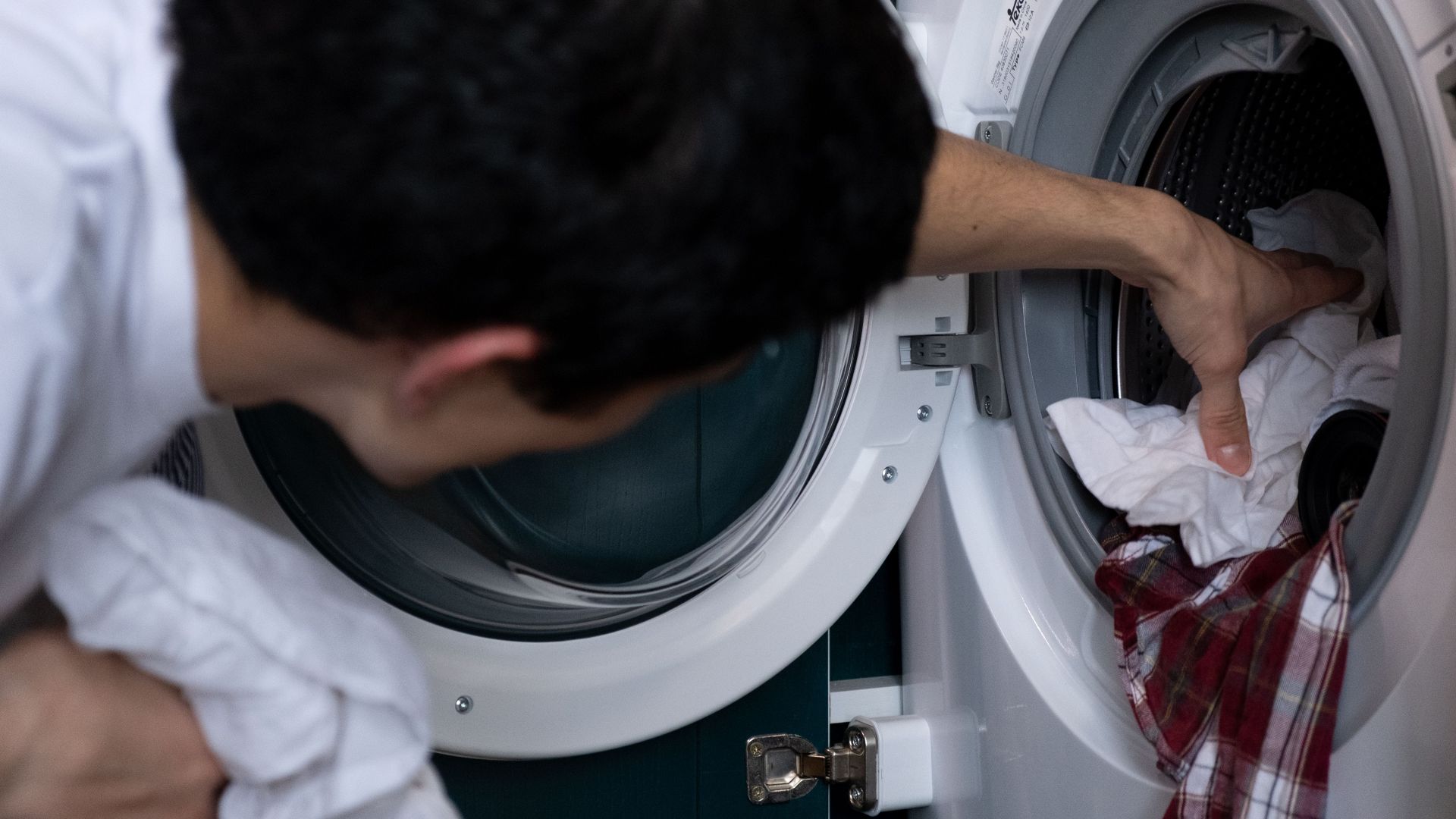Close-up of a man placing clothes into a washing machine during household chores.
