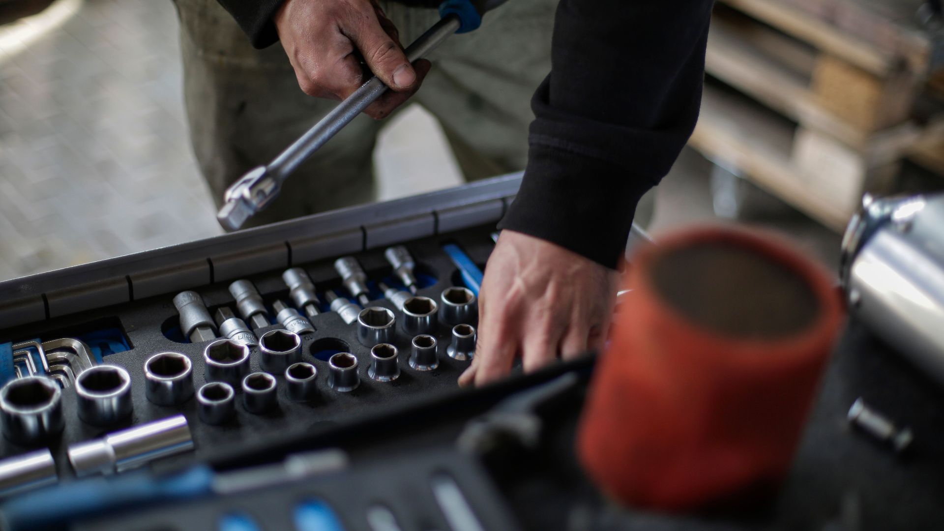 From above view of crop unrecognizable mechanic in workwear choosing metal sockets for ratchet while repairing vehicle in modern workshop