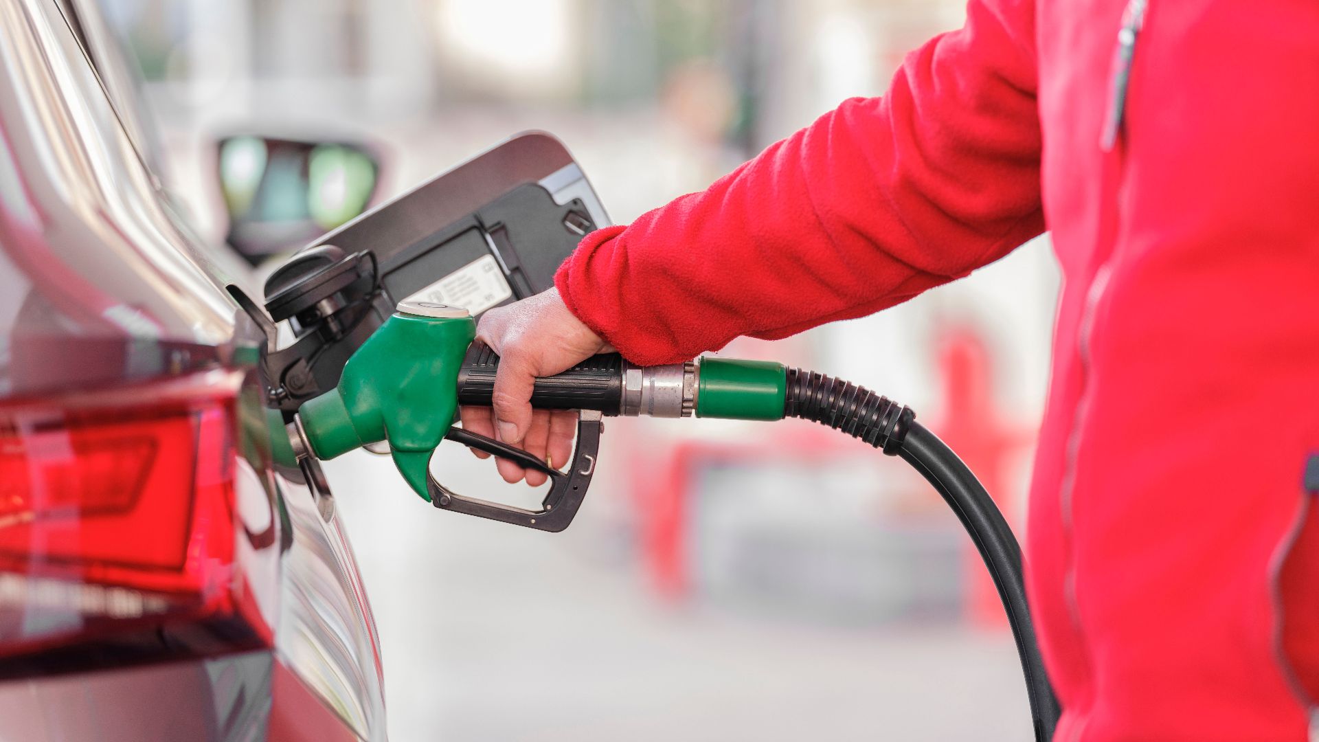 Close-up of a person refueling a car with a green hose at a gas station.