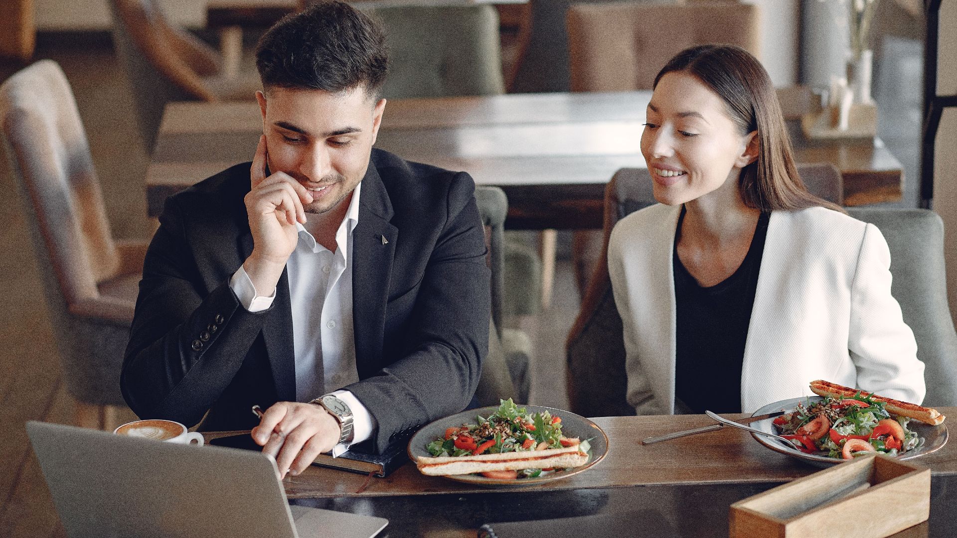Smiling multiracial business partners in formal wear sitting in cafe while working on project and using laptop
