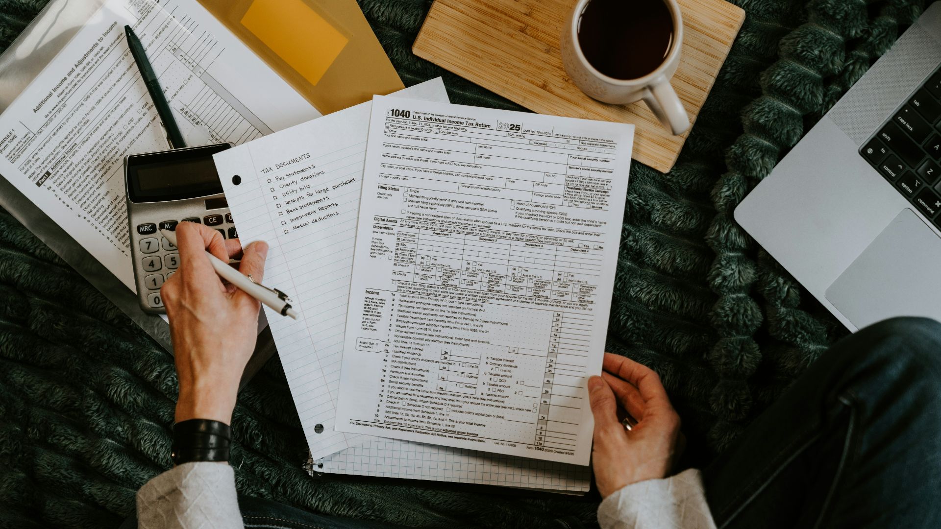 Person reviewing documents with calculator and laptop
