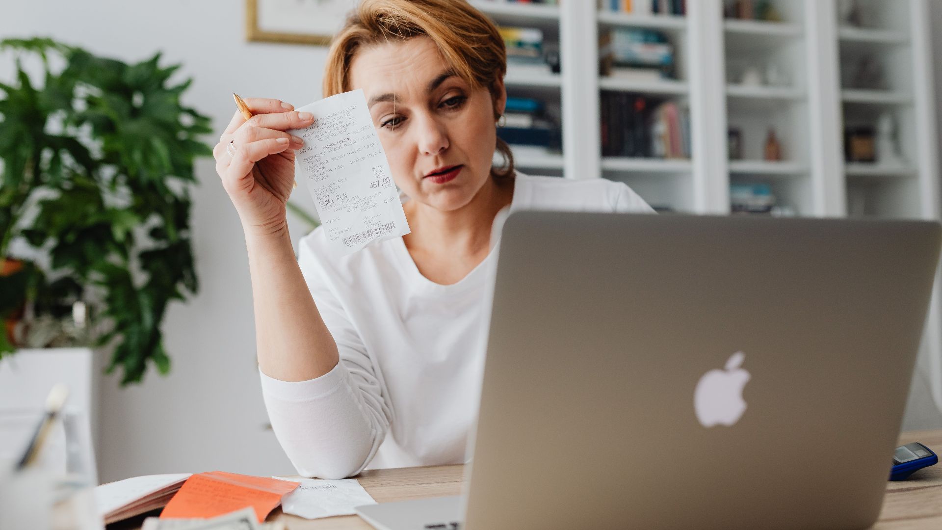 Woman concentrating on receipts while using a laptop, reflecting financial stress.