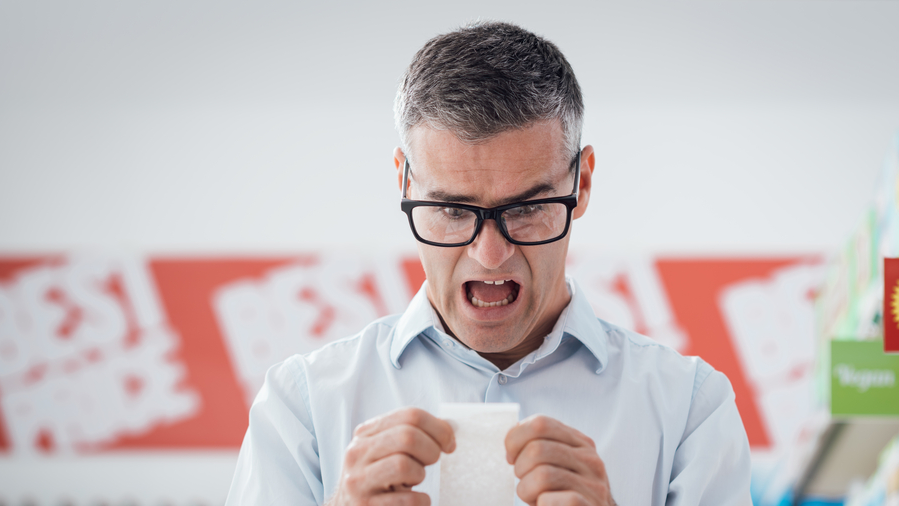 Shocked man doing grocery shopping at the supermarket and checking a long receipt