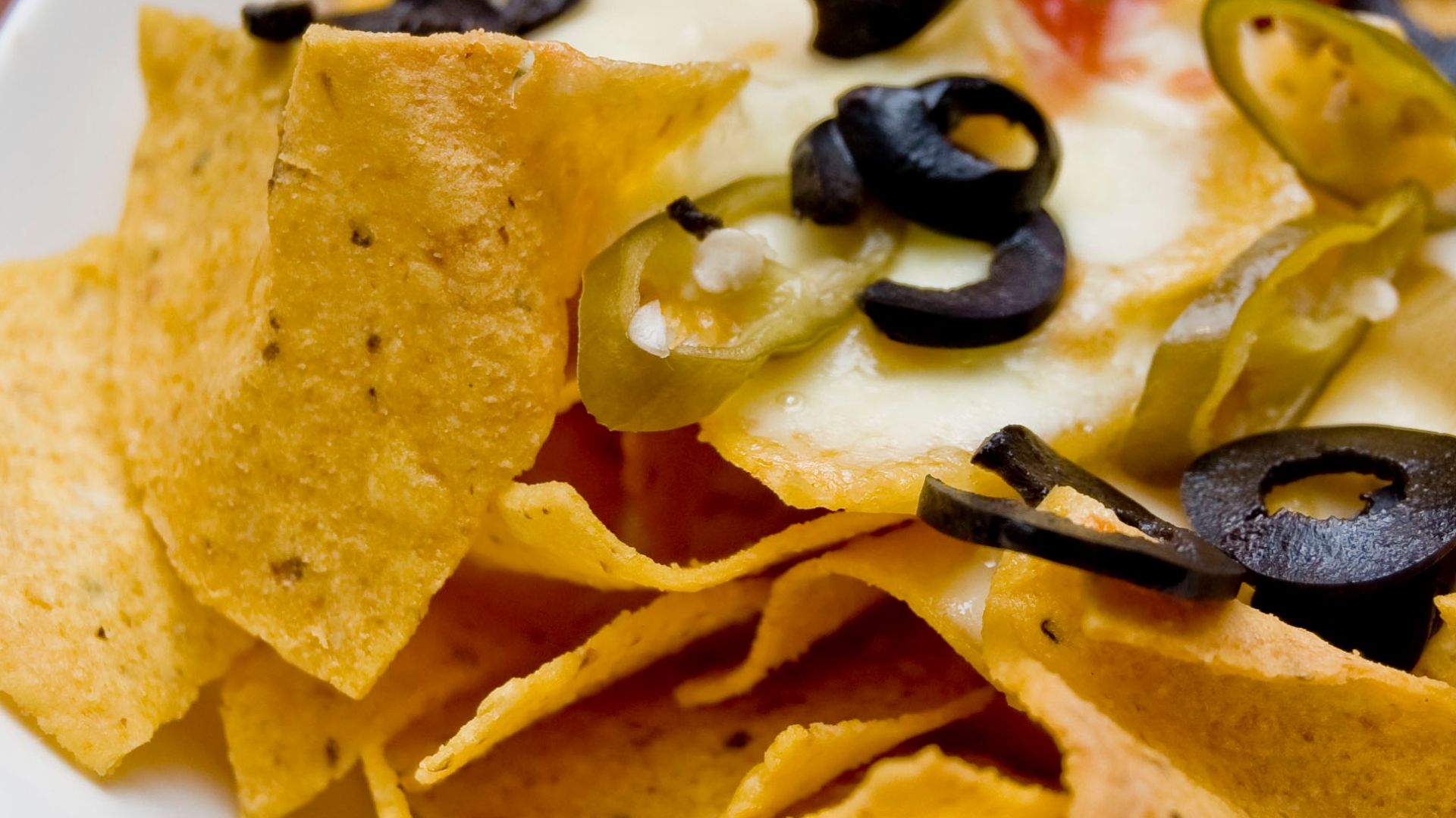 A plate of Nachos—tortilla chips topped with melted cheese, sliced chile peppers, sliced black olives, and chili sauce—as served by the Logenhaus Roast & Grill in the UEP Subang Jaya township of Selangor, Malaysia.Cheese Nachos
