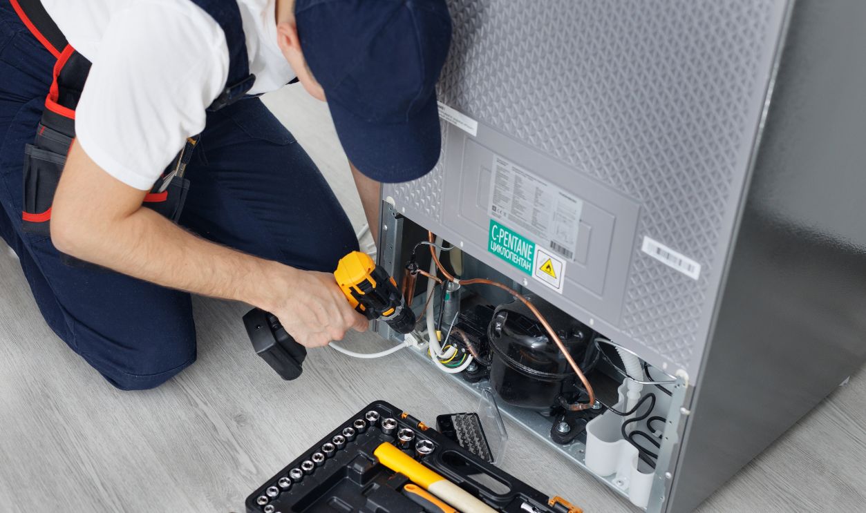Male technician repairs a refrigerator in the kitchen in close-up