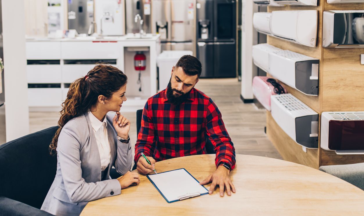 Young man with saleswoman in large modern household appliances store signing contract.