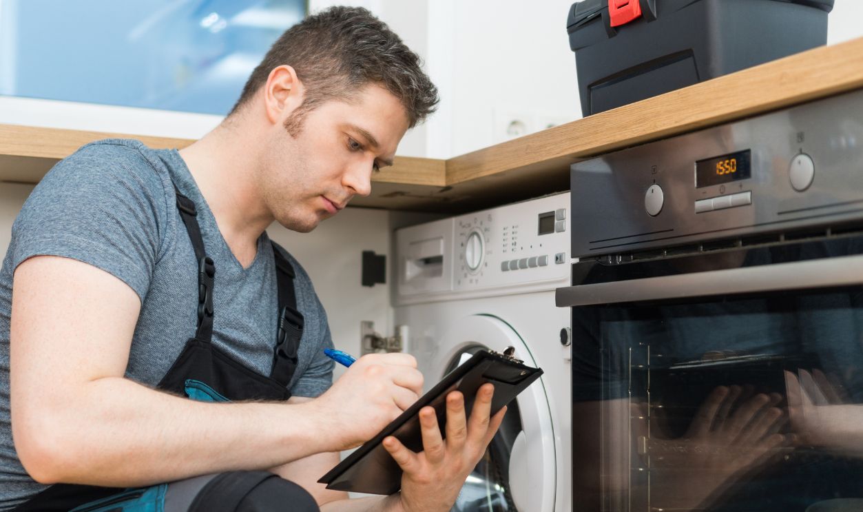 Handyman doing inspection of washing machine in the kitchen.