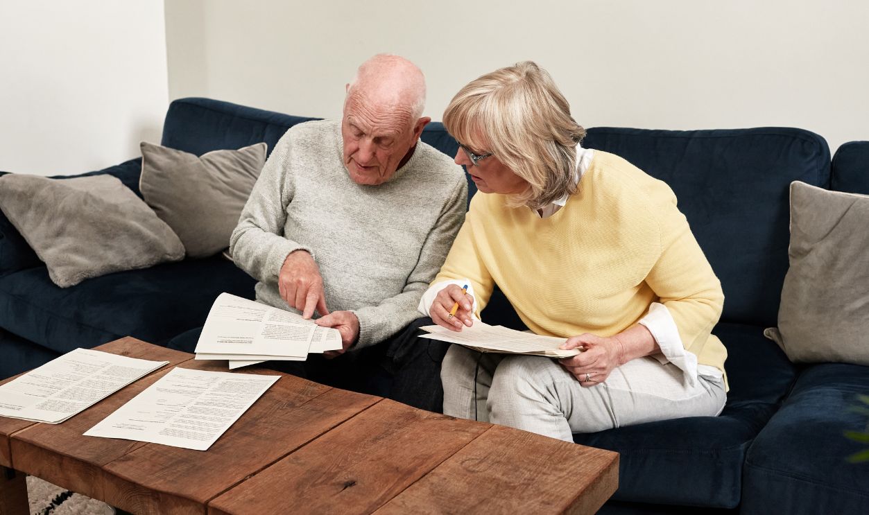 Senior couple reading documents in home for planning budget, financial assets and legal contract for insurance policy. Man, woman and paperwork of investment information, bills and retirement savings
