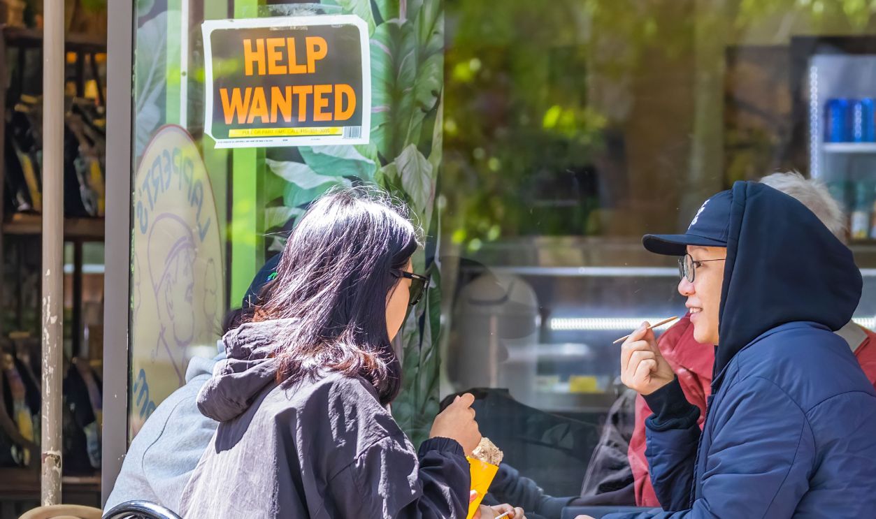 Three adults enjoy ice cream and conversation at an outdoor café with a 'Help Wanted'