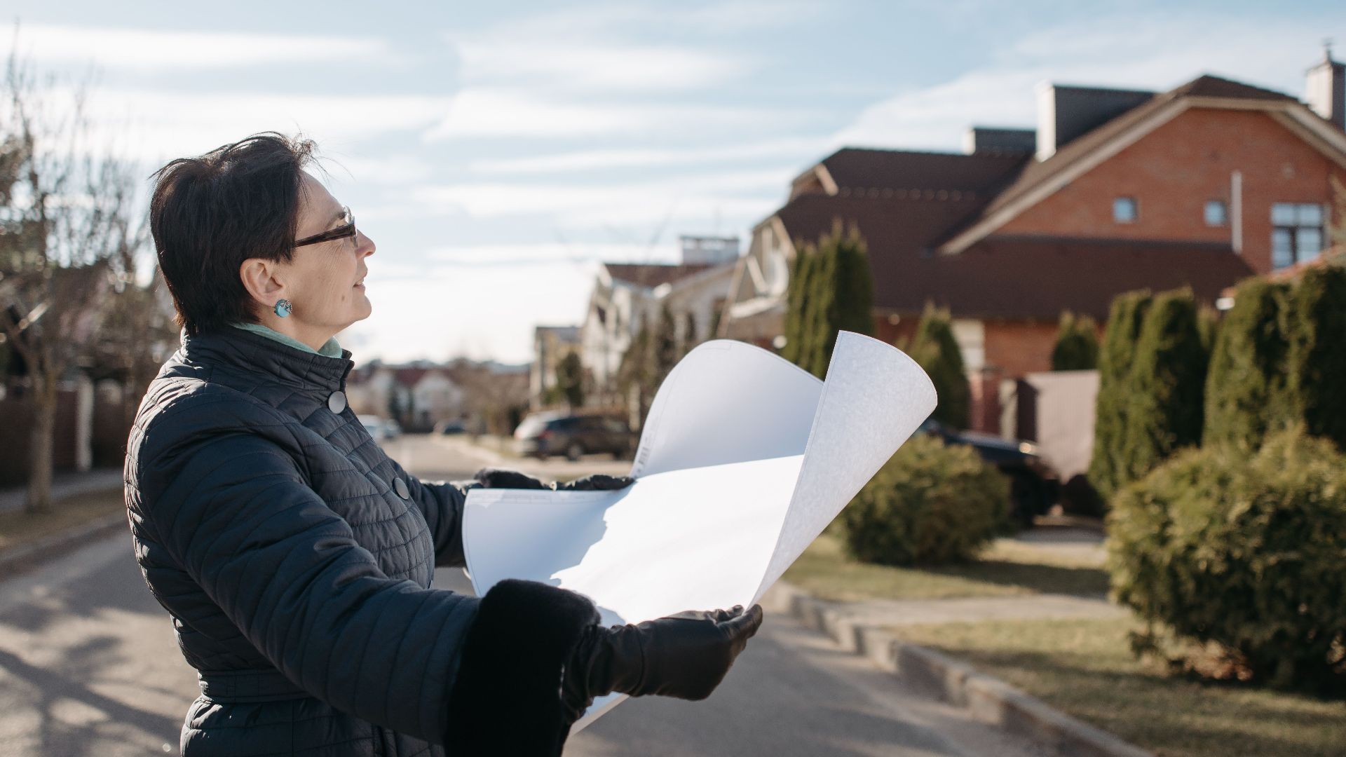 Woman in a blue jacket reviewing architectural plans outdoors on a sunny day.