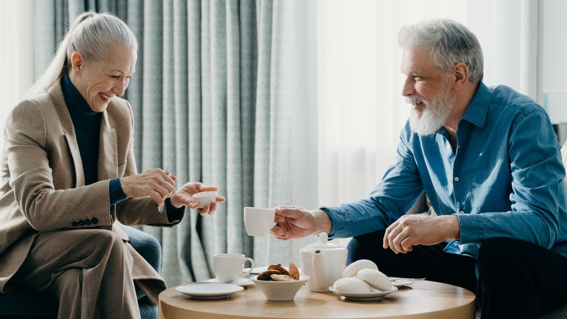 Elderly couple relaxing at home, enjoying a cozy moment with coffee and pastries.