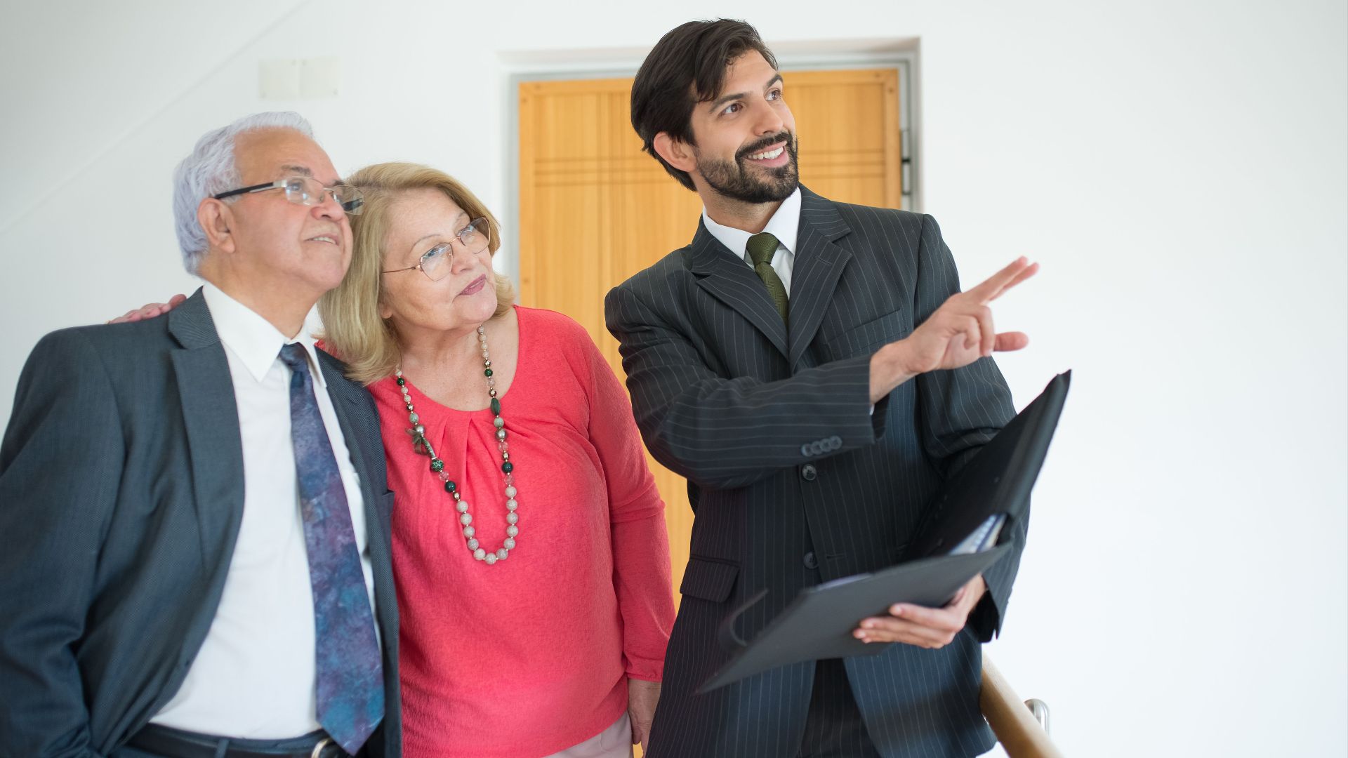 An elderly couple viewing a property with a realtor indoors, discussing real estate options.