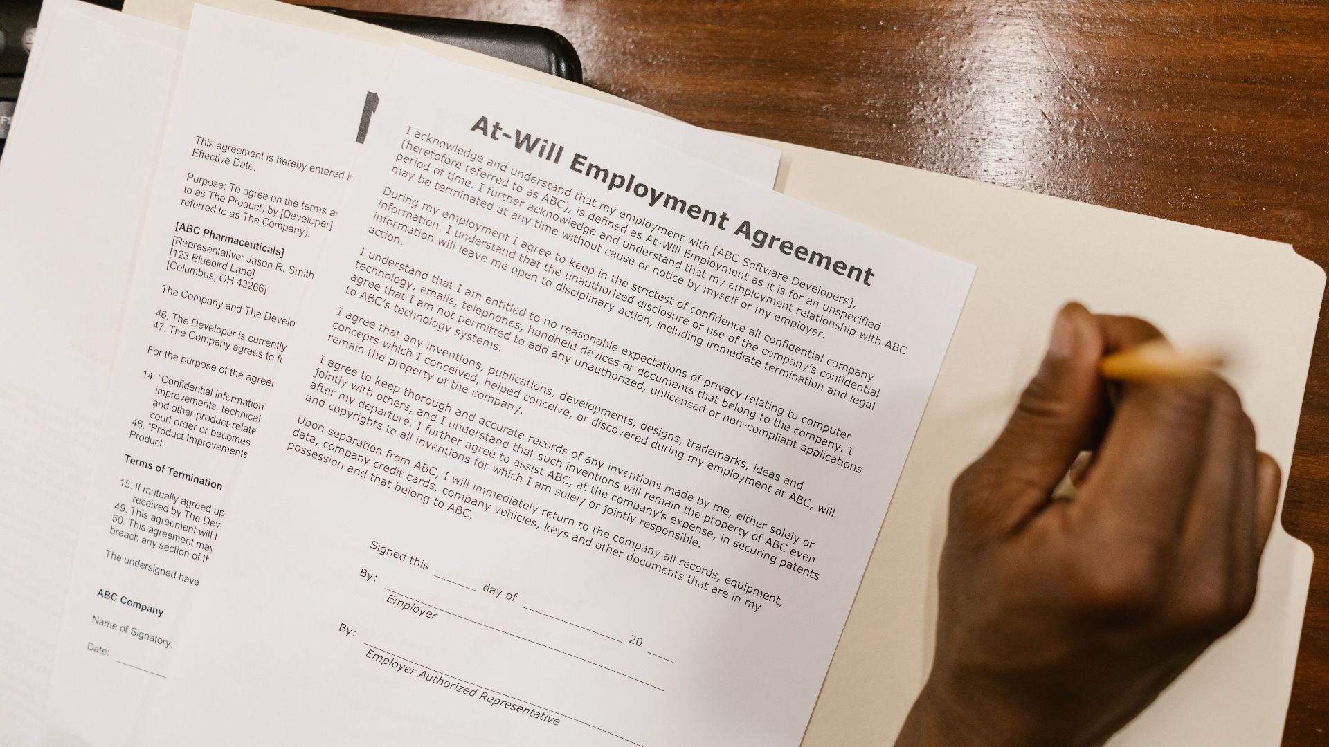 Close-up of a hand signing an at-will employment agreement on a wooden desk.