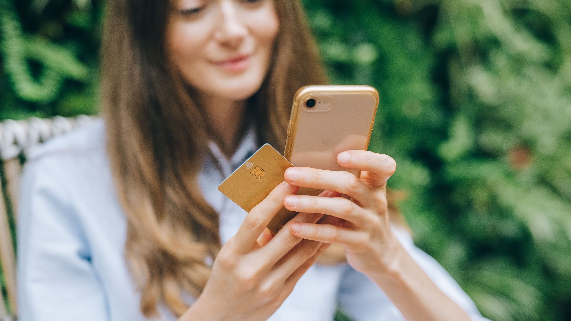 Woman using smartphone and credit card outdoors for online shopping.
