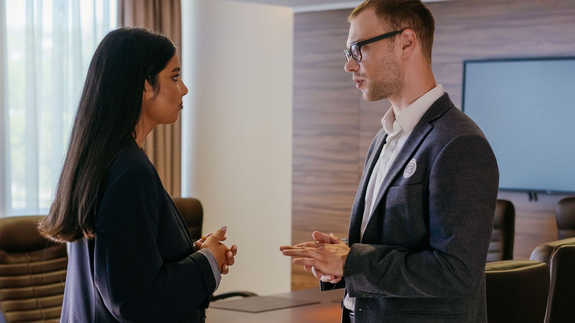 Two professionals engaged in discussion inside a modern conference room setting.