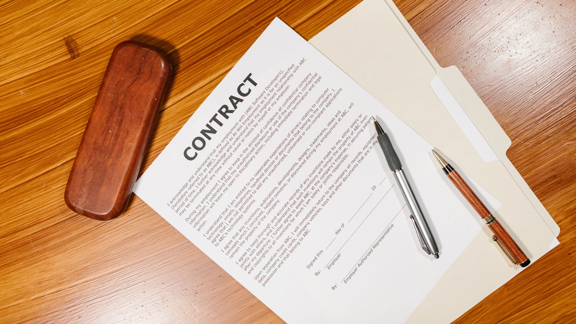High-angle view of a contract document with pens and a case on a wooden table.