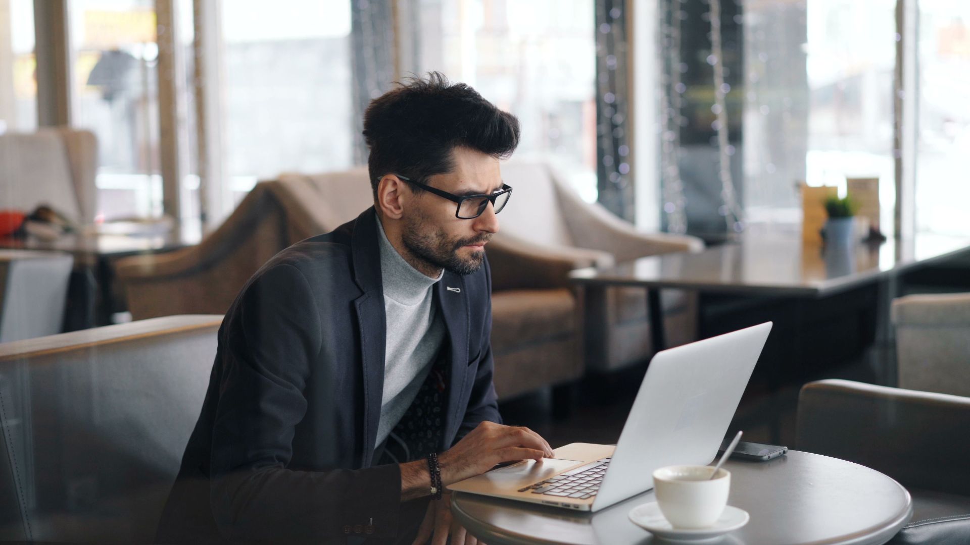 Focused businessman working on a laptop in a stylish café, drinking coffee.