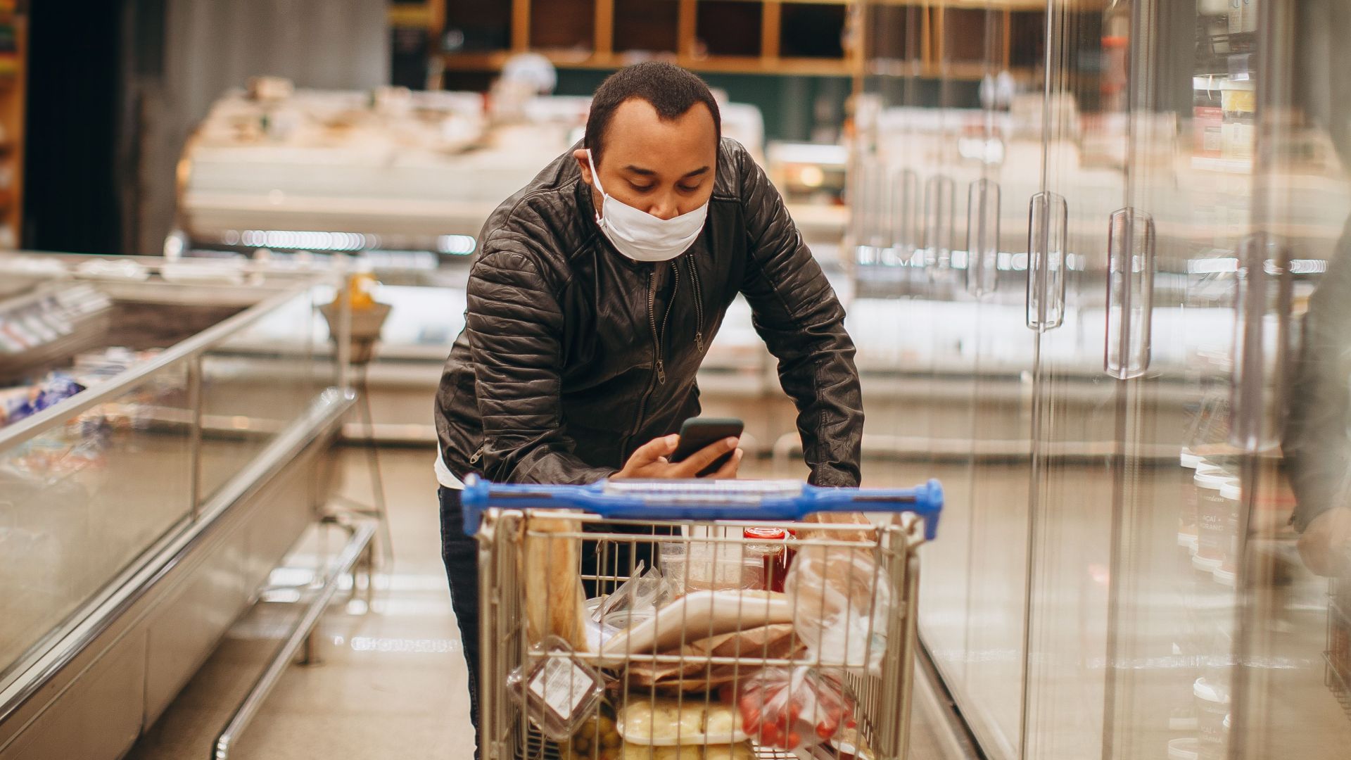 Man wearing mask shops in a supermarket, pushing a cart in the aisle.