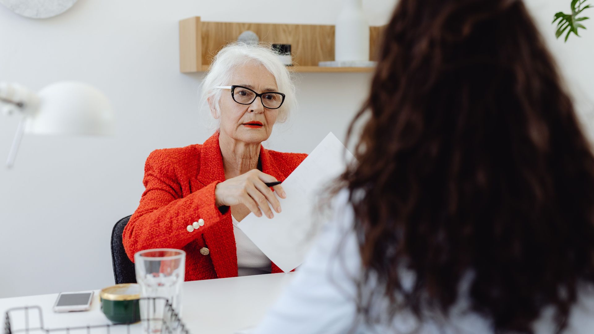 Senior businesswoman in red blazer engaging in a document review meeting in a modern office setting.