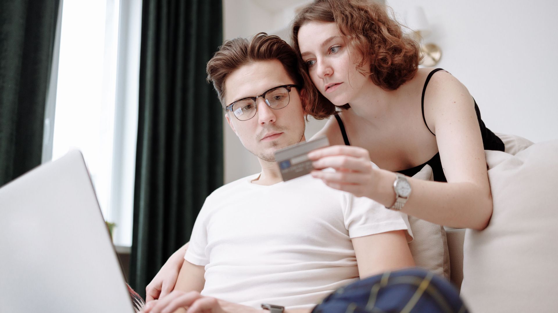 A young couple using a laptop and credit card for online shopping indoors.