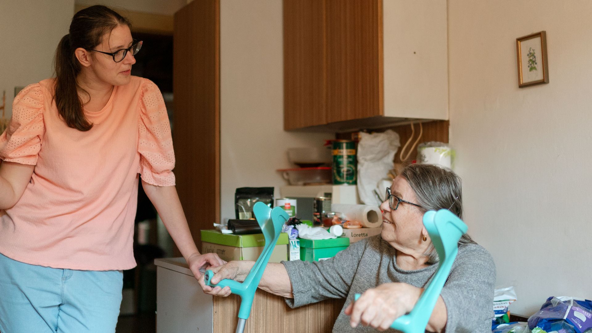 A caregiver engaging with a senior using crutches in a cozy Prague home environment.