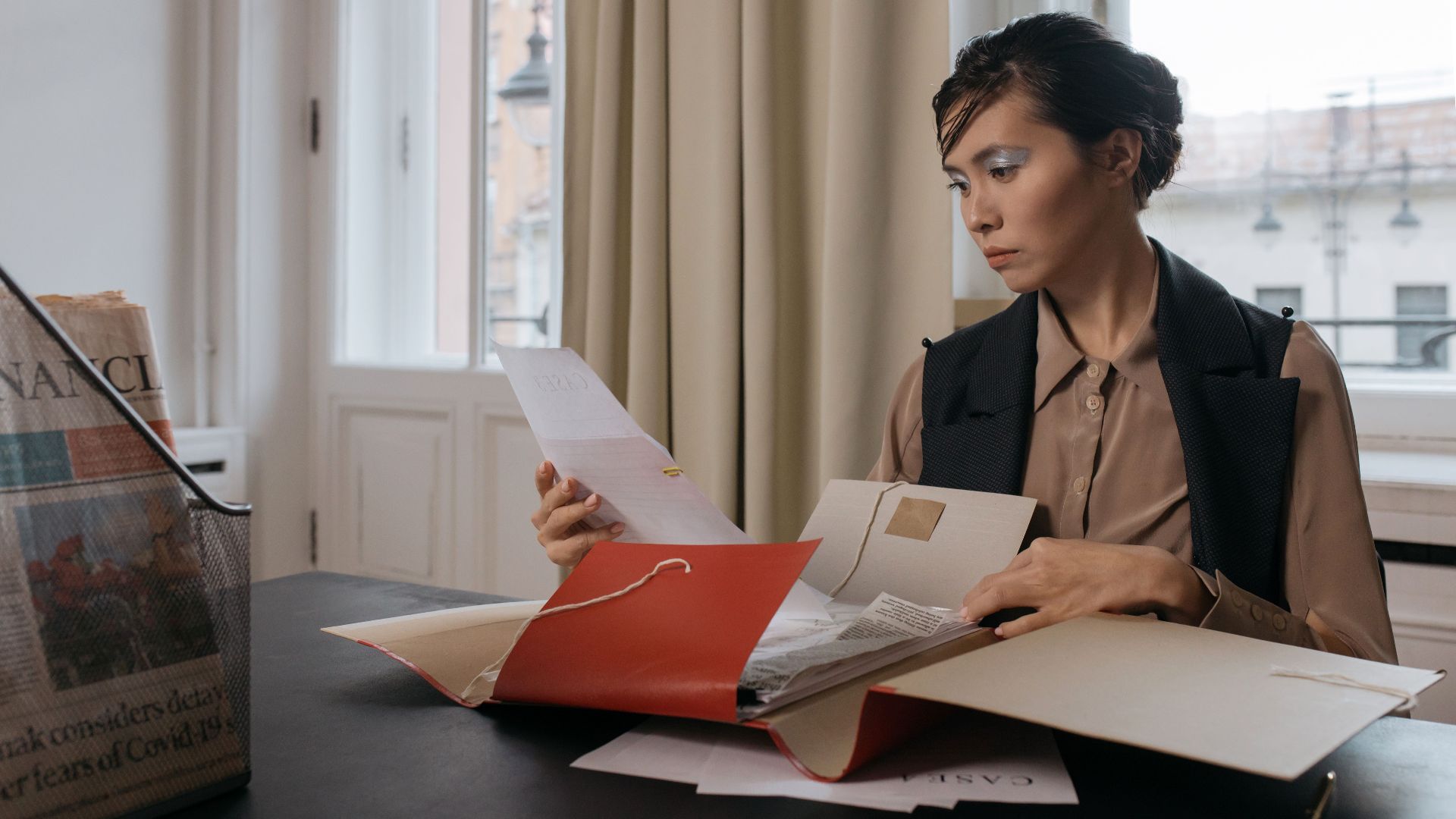 Businesswoman in an office setting reviewing important documents from a red folder with focus and determination.