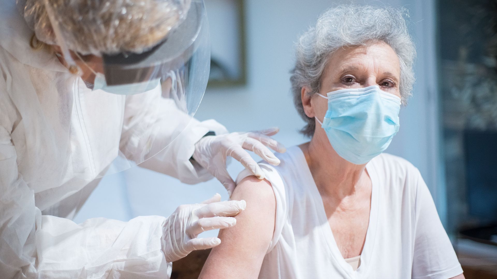 Senior woman wearing a mask getting vaccinated by a healthcare worker in PPE.