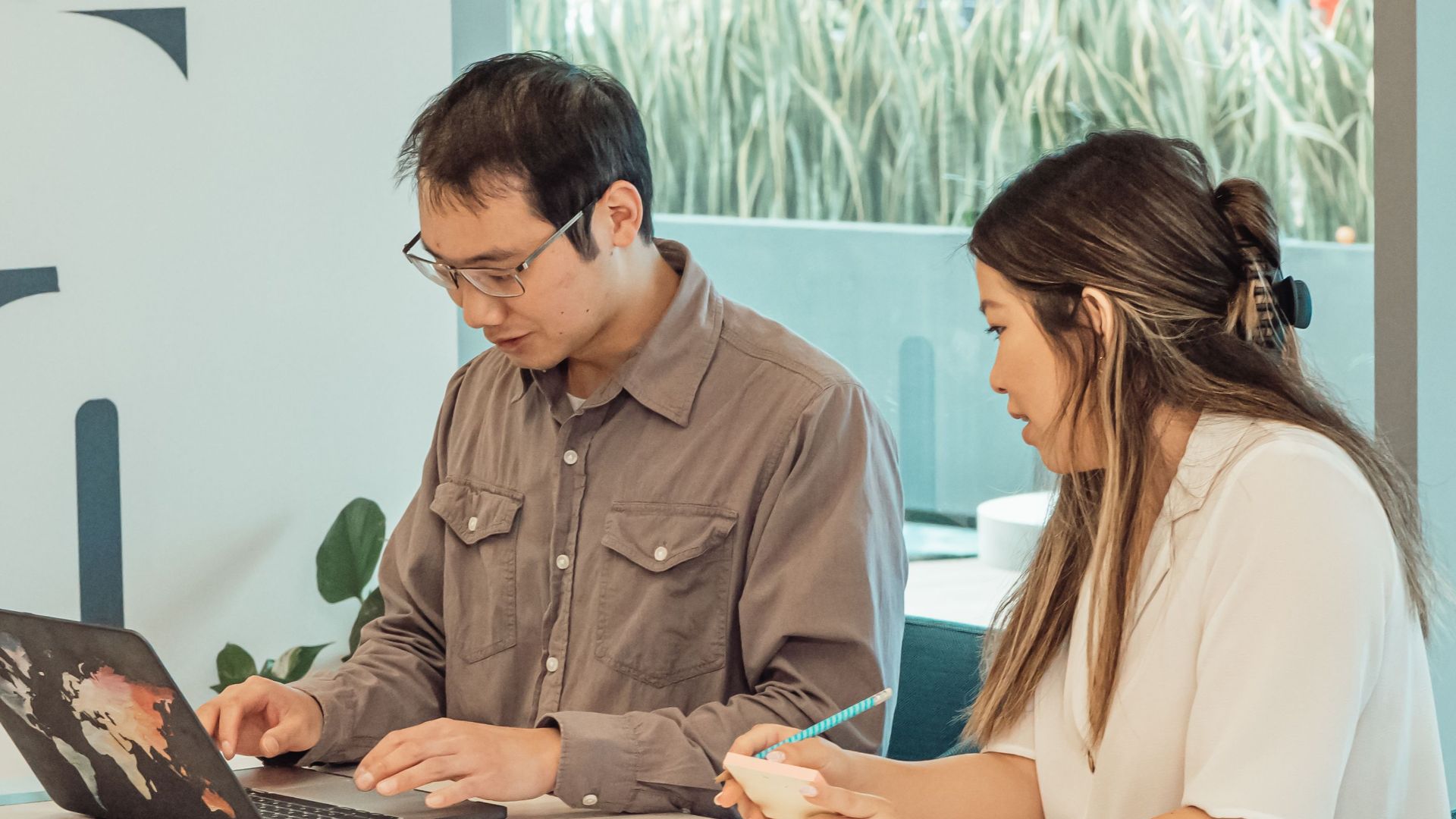 Two colleagues collaborating in a modern office setting over a laptop and documents.