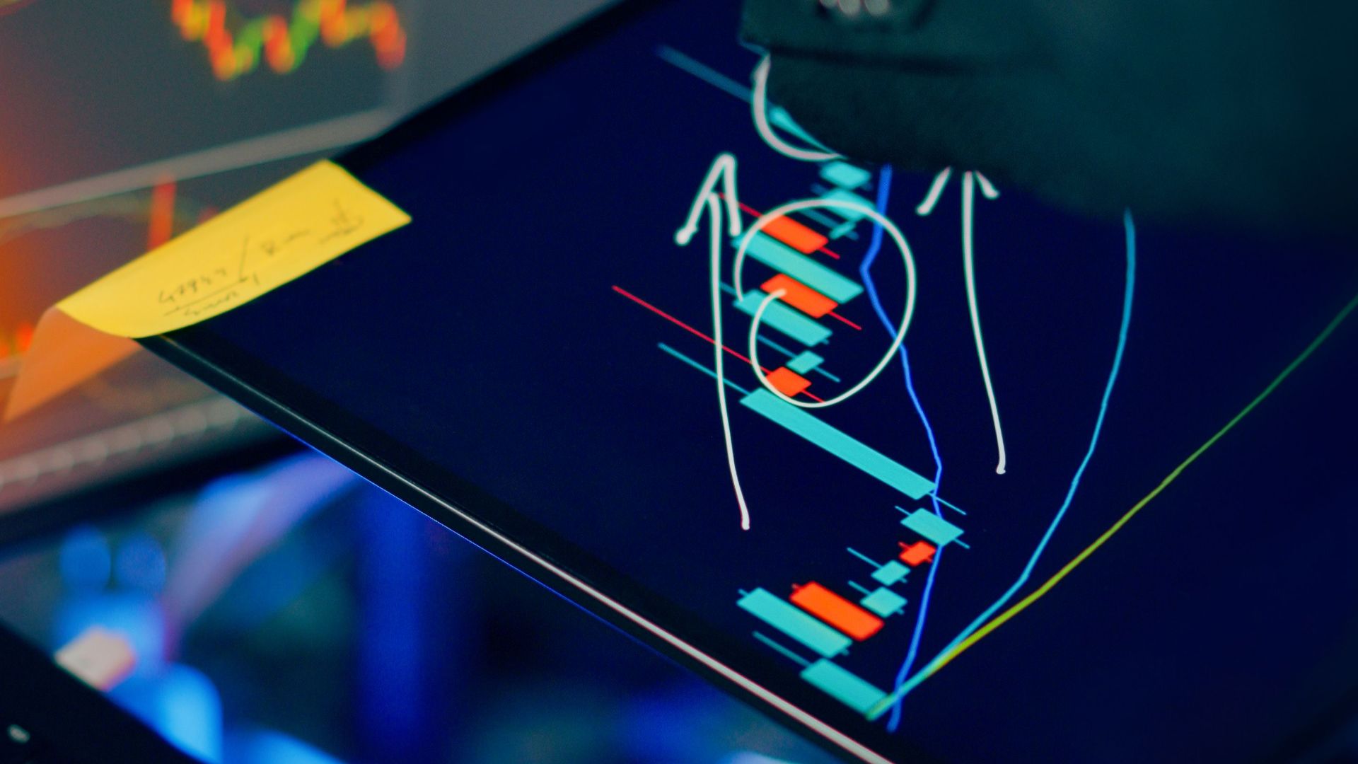 A business professional examines financial charts on a tablet and monitor for investment strategy.