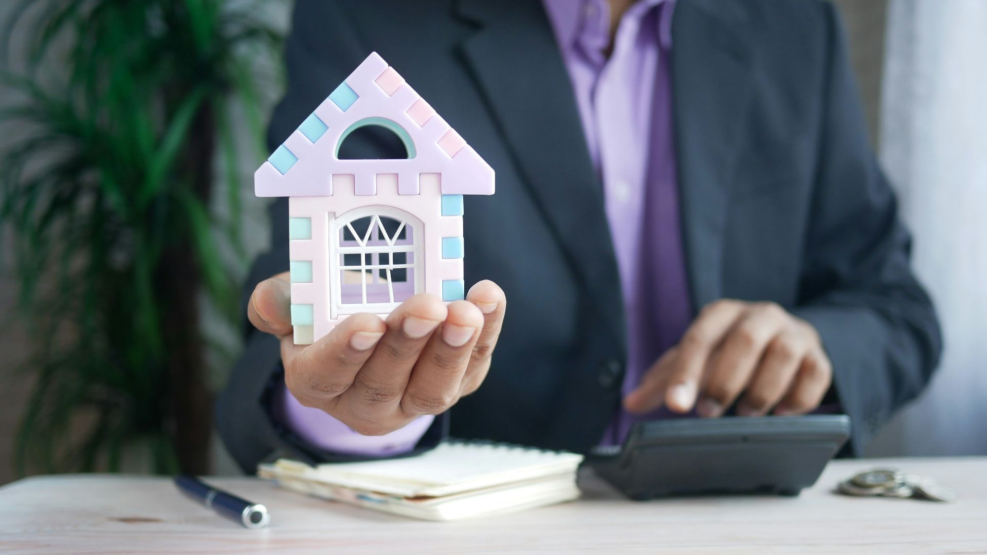 man holding model house at desk with calculator