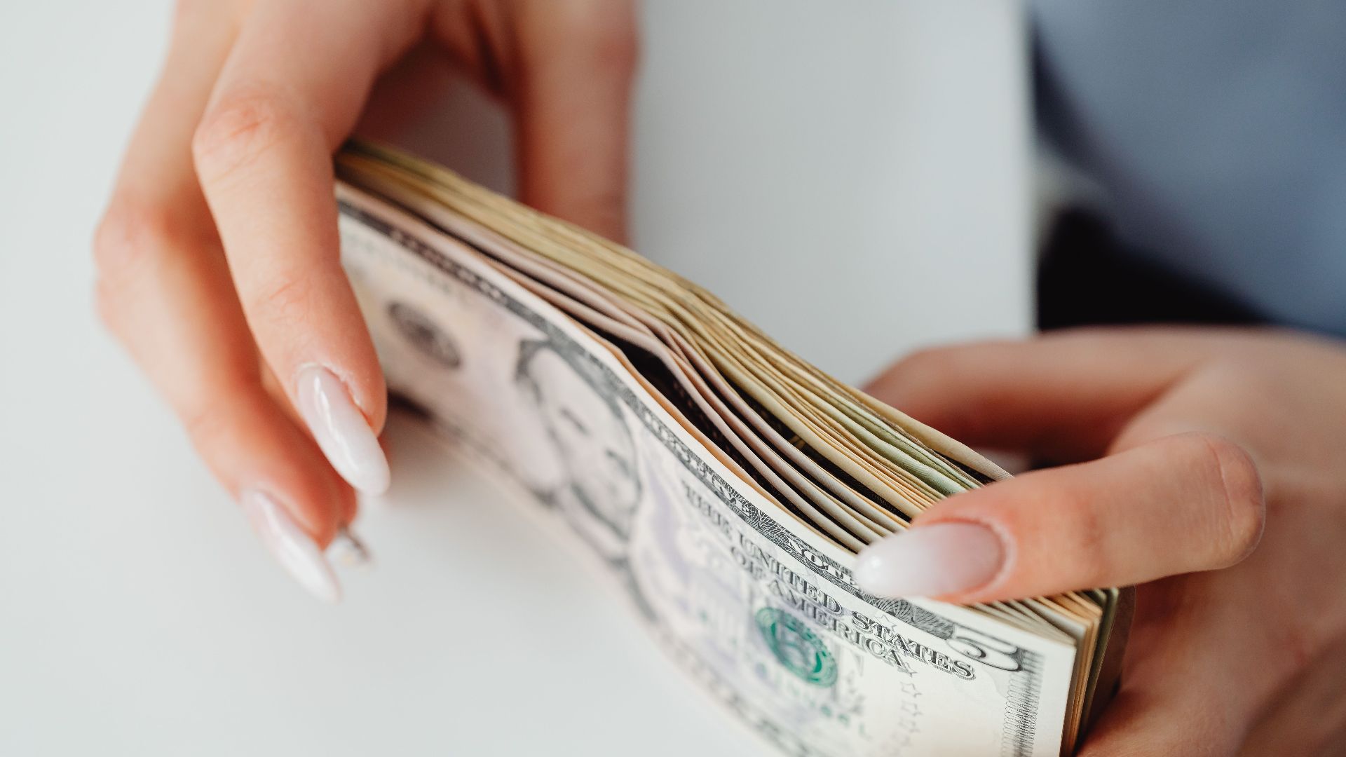 Hands carefully holding a stack of US dollar bills, representing finance and currency.