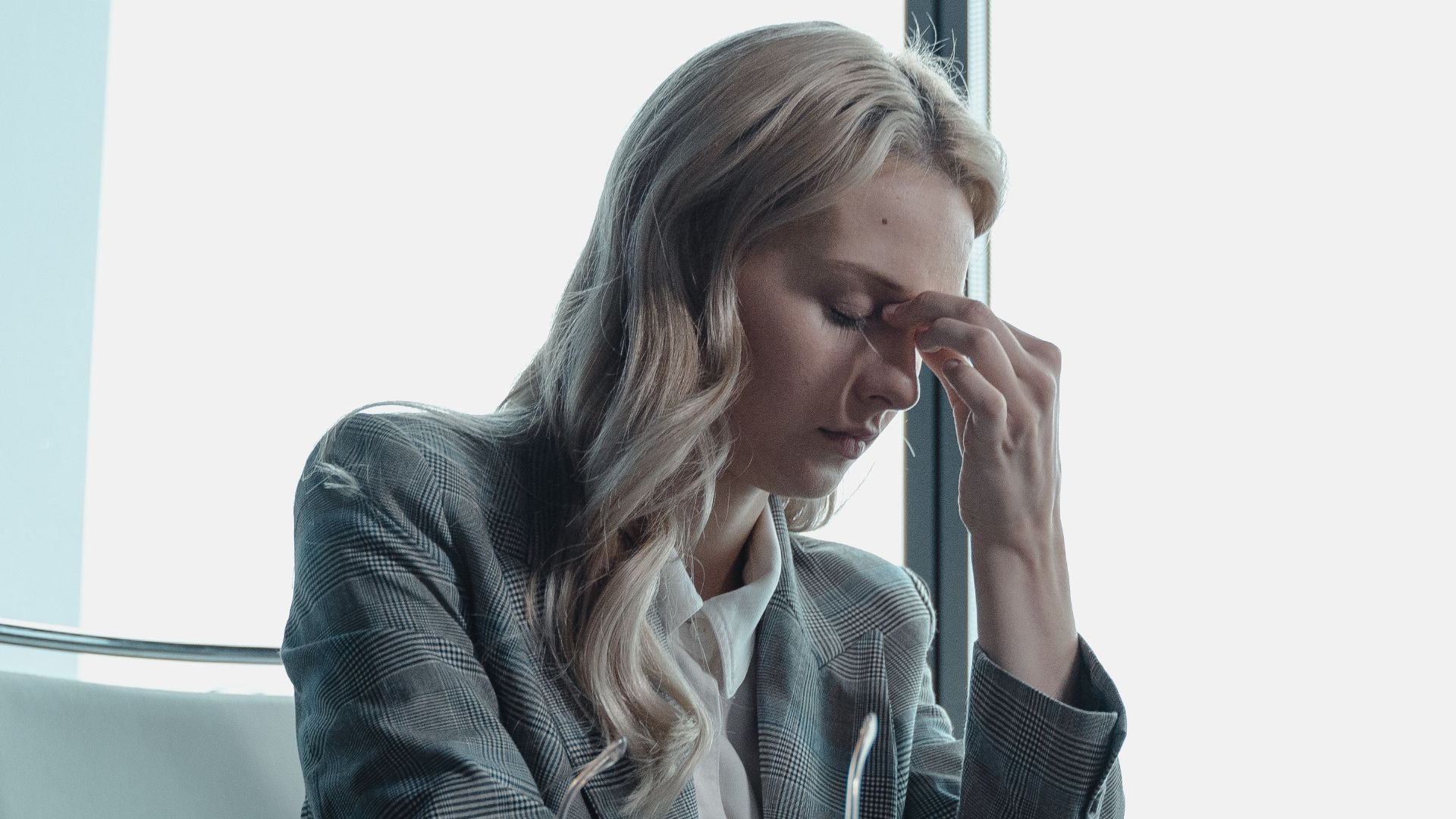 Professional woman in office, sitting at desk, looking stressed with laptop.