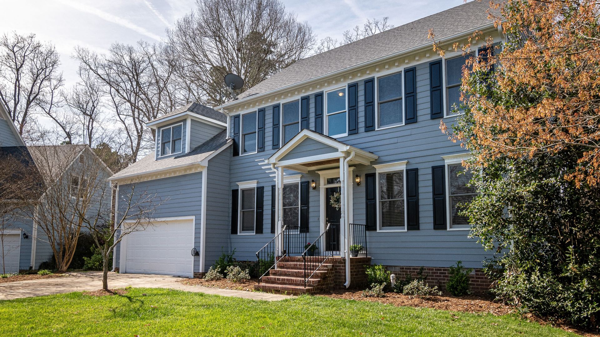 Spacious blue family home with garage, surrounded by trees and lush lawns in a suburban neighborhood.