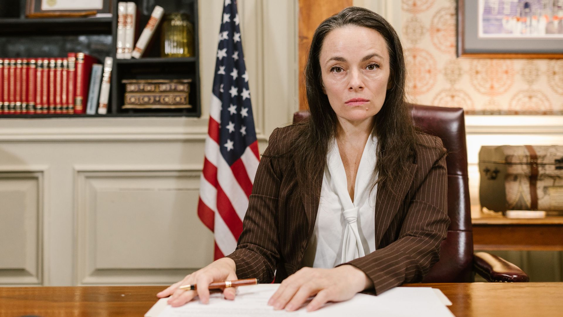 Confident female lawyer at her desk in a law office with legal books and the American flag.