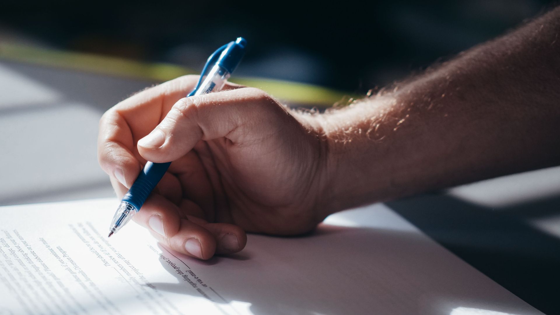 Detailed shot of a hand holding a blue pen while signing a document. Ideal for legal and business themes.