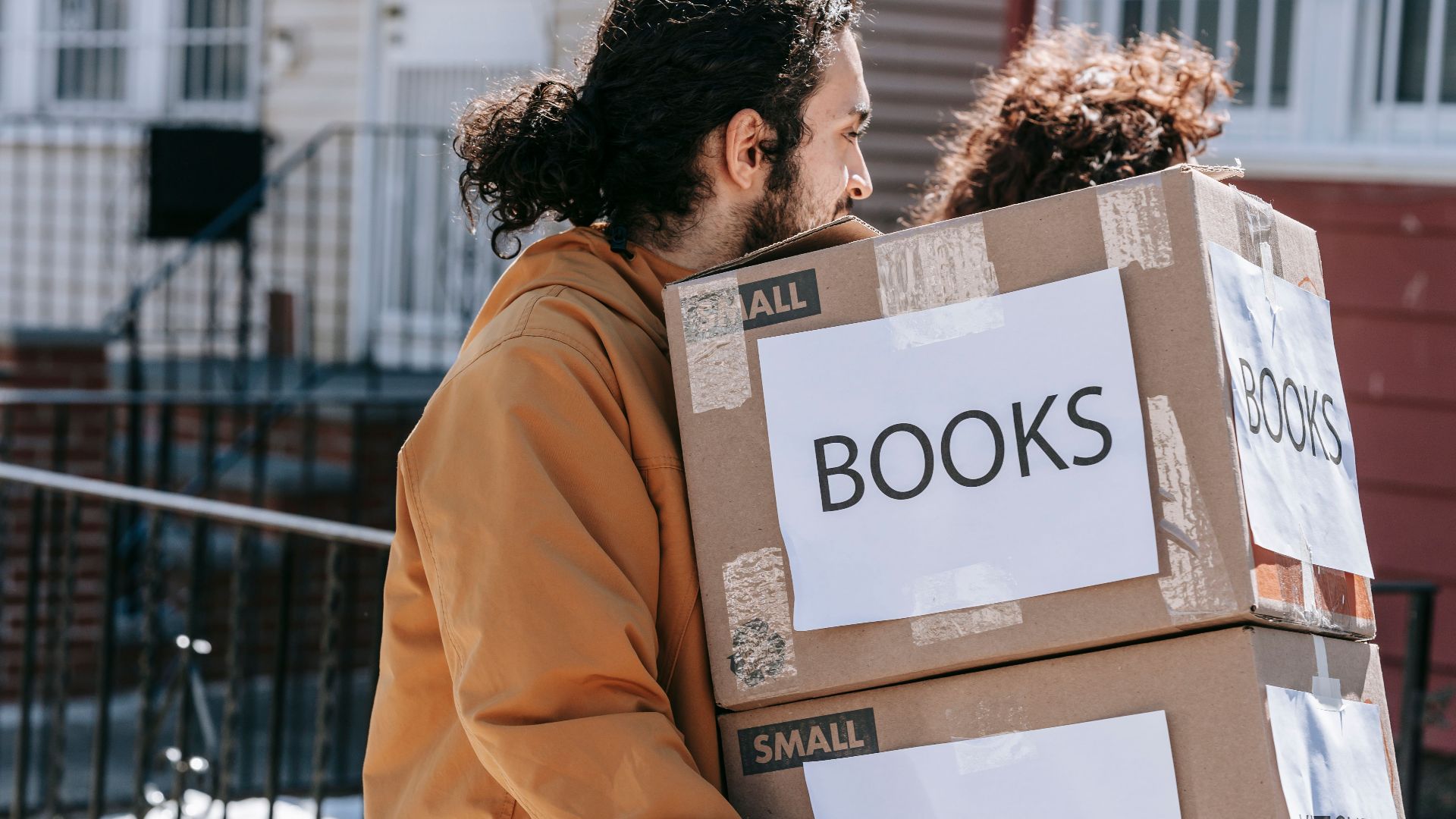 A couple carrying labeled boxes outside, symbolizing moving to a new home.