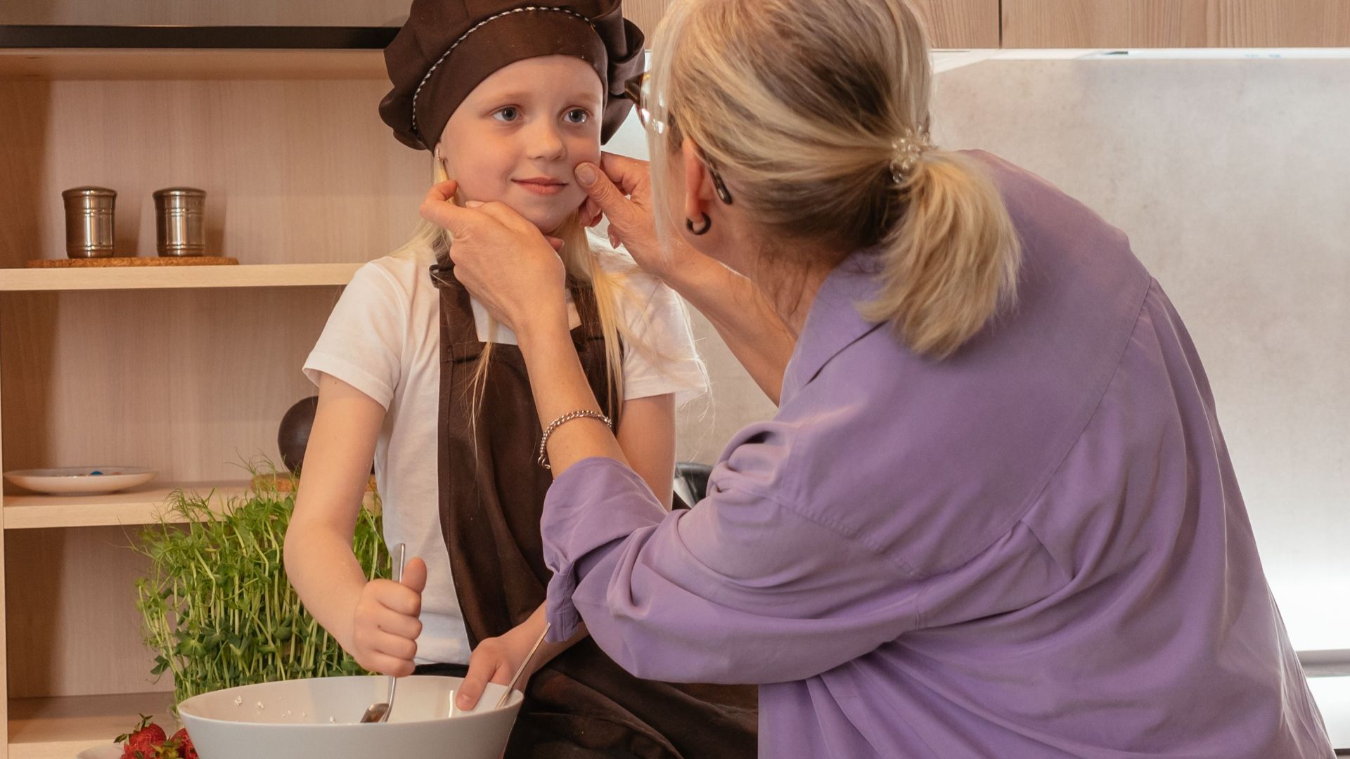 An elderly woman and her grandchild share a joyful moment cooking in the kitchen together.