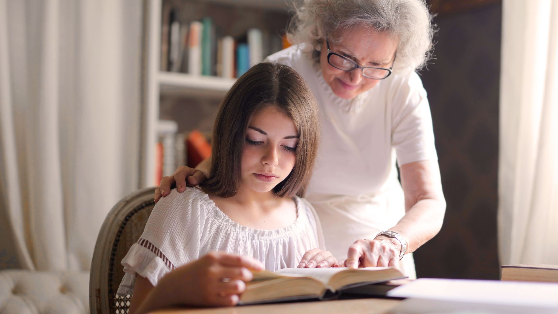 A grandmother and young girl reading a book together in a cozy indoor setting, fostering education and bonding.