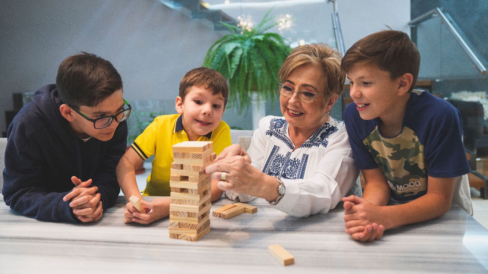 A joyful family moment with grandma and grandsons playing Jenga indoors, capturing quality time together.