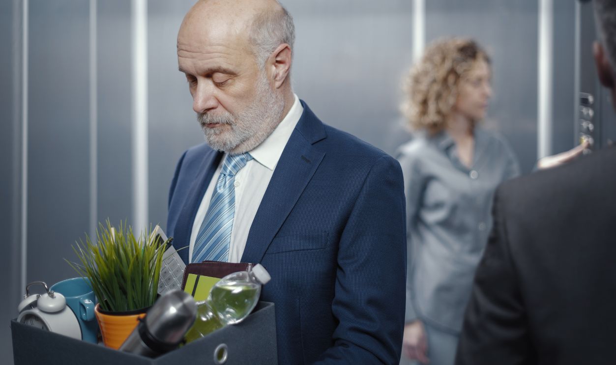 Frustrated senior businessman carrying his belongings in a box and getting off the elevator after losing his job