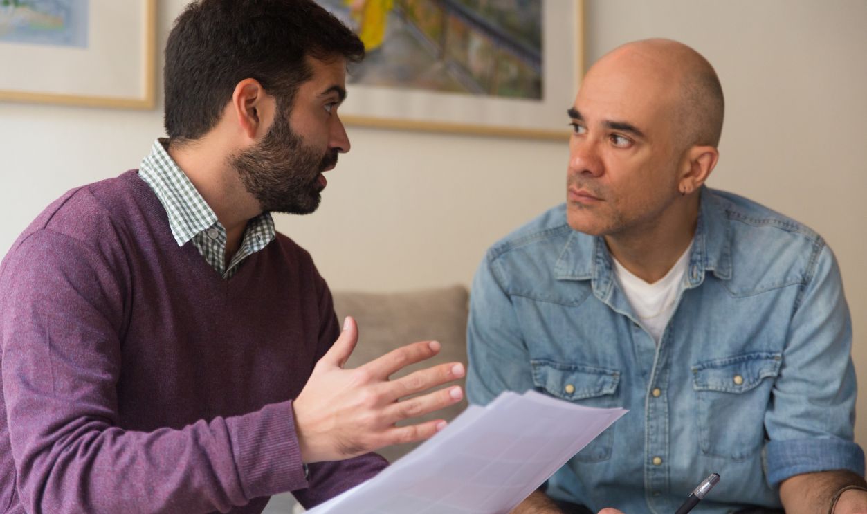 Professional and client meeting and discussing documents. Two men with papers sitting in living room at home and talking. Expertise concept